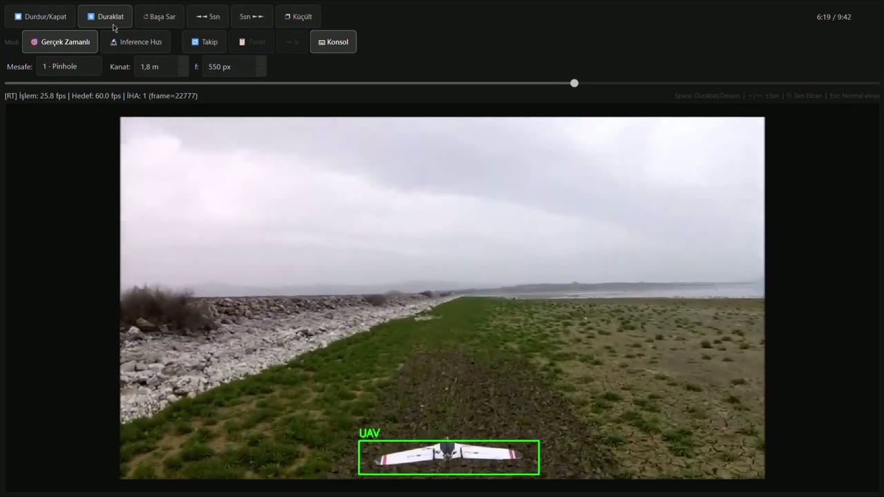 Takip kapalı: çimenlik bir pistte, kameraya yakın bir sabit kanatlı İHA yeşil, kimliksiz bir UAV kutusunda.